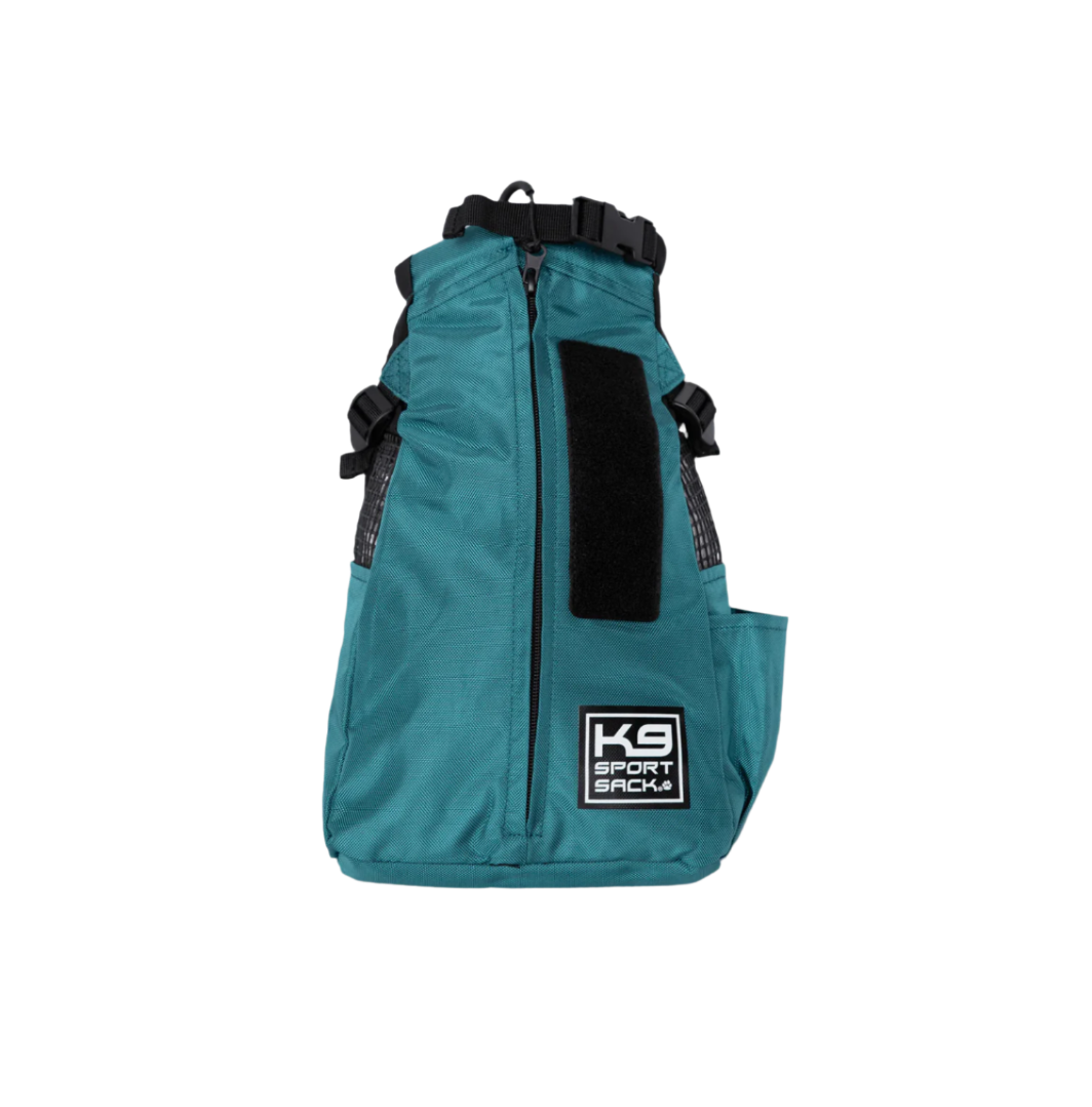 A green K9 Sport Sack dog carrier backpack with black straps and a brand logo on the front.