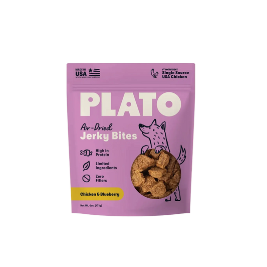 A purple stand-up pouch of PLATO Air-Dried Jerky Bites, Chicken & Blueberry flavor, on a light cream background. The packaging features a cartoon illustration of a dog and a clear window showing the brown jerky pieces inside.
