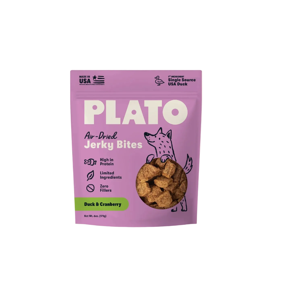 A purple stand-up pouch of Plato Air-Dried Jerky Bites, Duck & Cranberry flavor, shown against a light cream background. The packaging features a cartoon fox and a circular cutout displaying the brown jerky pieces inside.