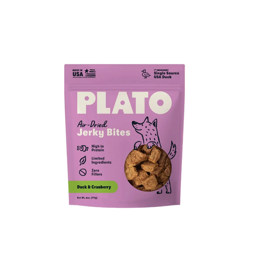 A purple stand-up pouch of Plato Air-Dried Jerky Bites, Duck & Cranberry flavor, shown against a light cream background. The packaging features a cartoon fox and a circular cutout displaying the brown jerky pieces inside.