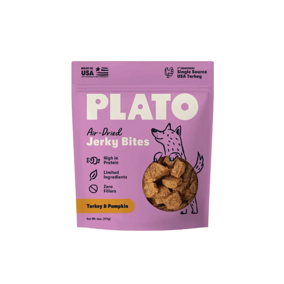 A purple stand-up pouch of Plato Air-Dried Jerky Bites, Turkey & Pumpkin flavor, shown against a light cream background. The packaging features a cartoon dog illustration and a clear window displaying the brown jerky pieces inside.