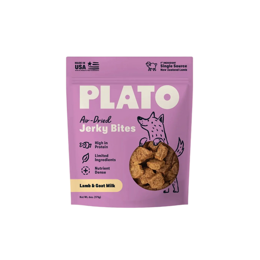 A purple stand-up pouch of Plato Air-Dried Jerky Bites for dogs, featuring a cartoon fox illustration and a circular window showing the brown jerky pieces inside. The packaging highlights 'Lamb & Goat Milk' flavor and includes 'Made in USA' and 'Single Source New Zealand Lamb' claims.