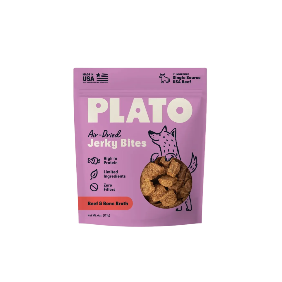 A package of Plato Air-Dried Jerky Bites for Beef & Bone Broth, featuring a light purple pouch with white text, a cartoon dog illustration, and a clear window showing the brown jerky inside, set against a solid cream background.