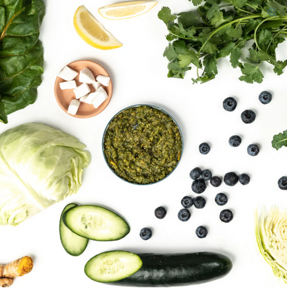 Assorted fresh vegetables and fruits including kale, lemon, blueberries, and cucumbers on a white background.