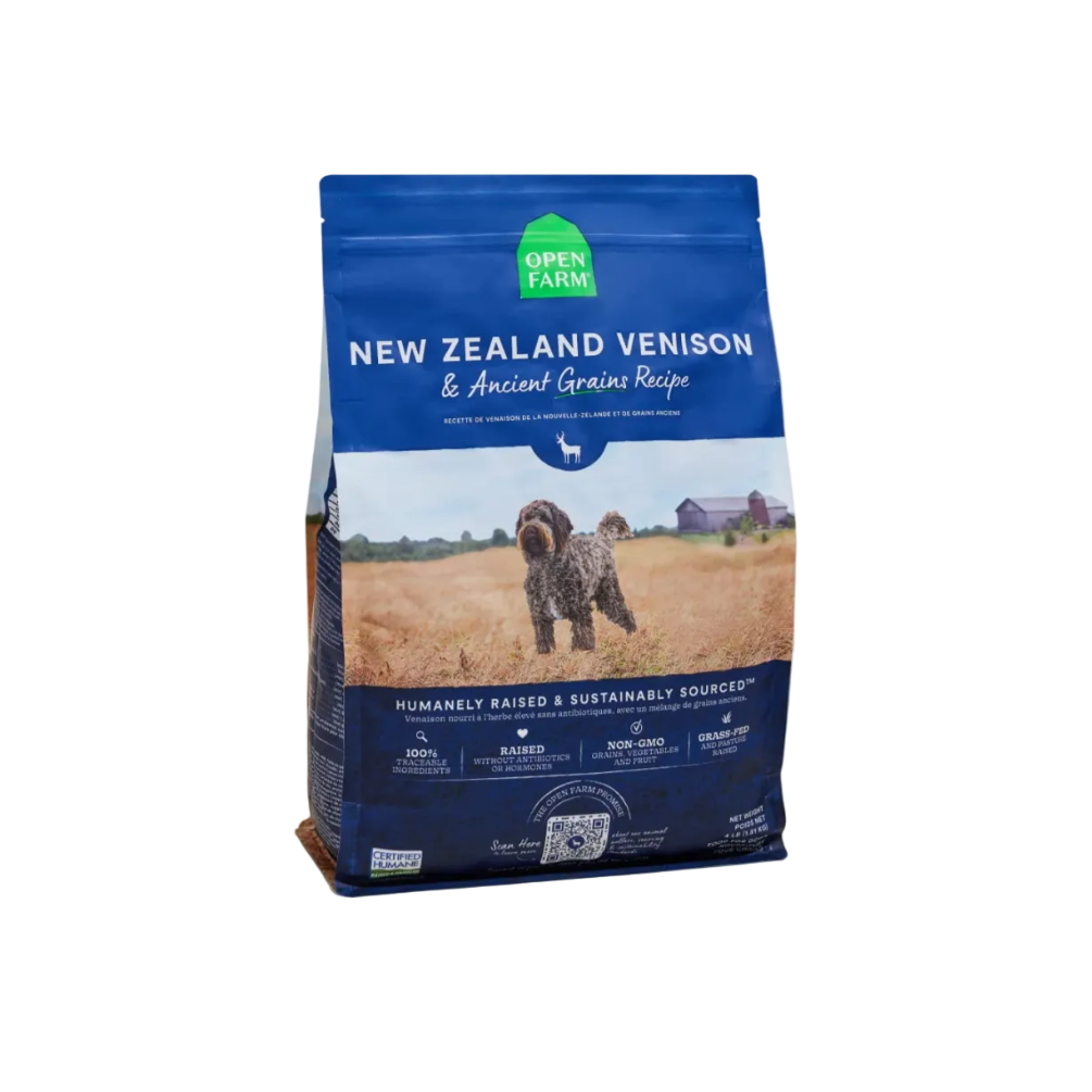 A bag of Open Farm New Zealand Venison & Ancient Grains Recipe dog food, featuring a blue package with a photo of a dog in a field, set against a solid beige background.